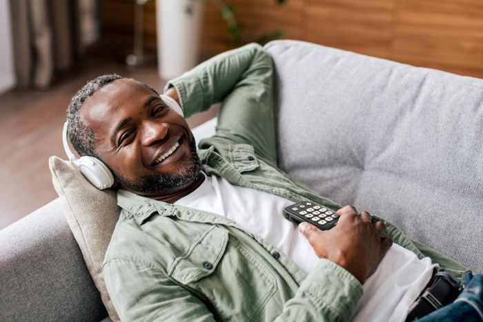 Image of a man laying on a couch with headphones on, smiling, while holding the stream 3 