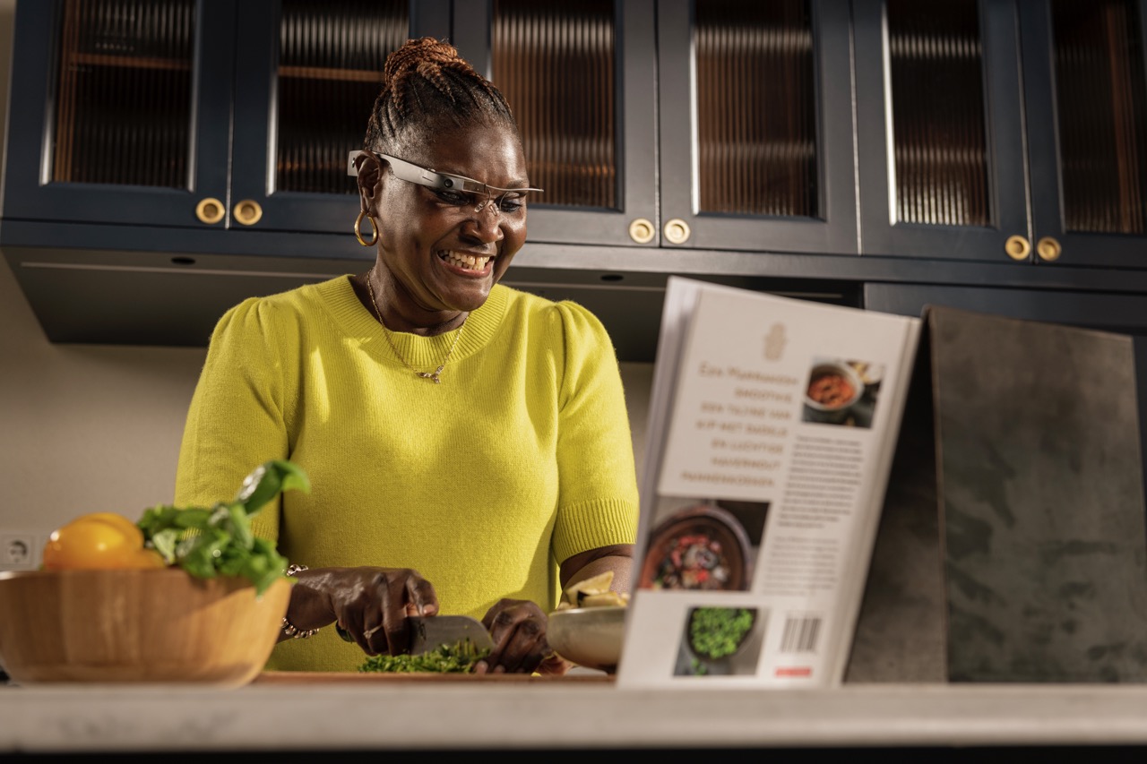 Woman wearing Envision glasses, wearables for low vision, and blind, to read a recipe off a cook book and making it