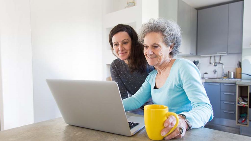 photo of an older woman and her daughter sitting at a kitchen counter top viewing on the older woman's laptop