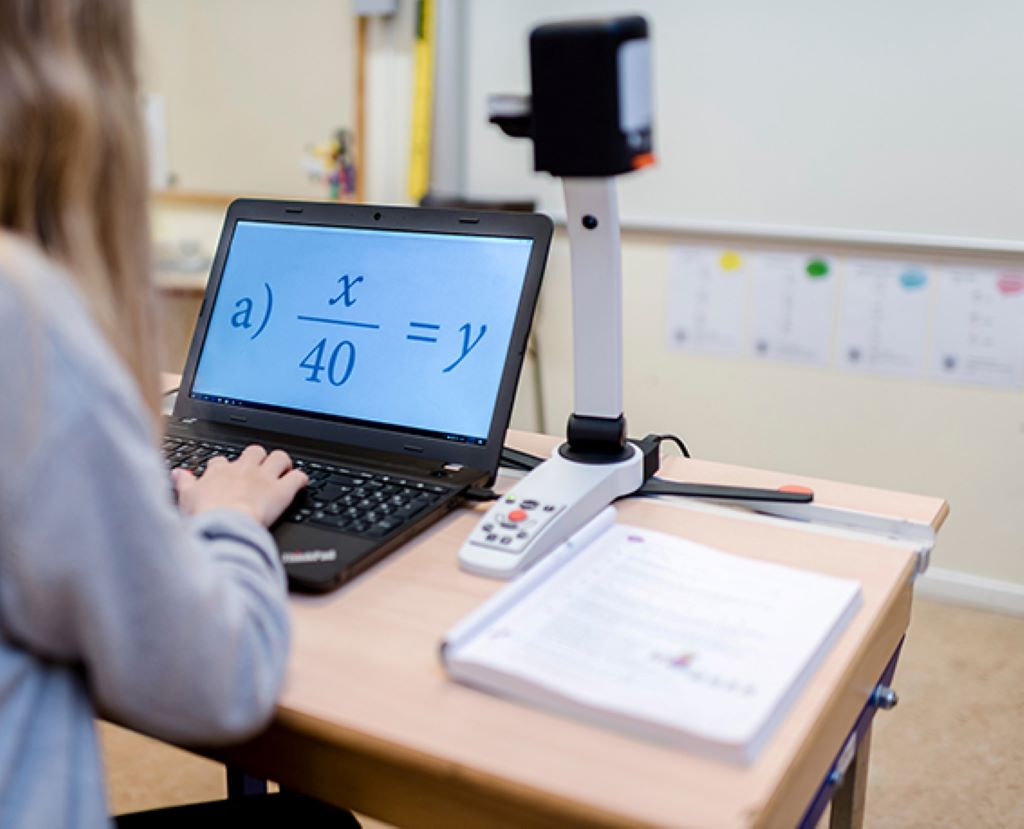 Image of a student using the MagniLink S Premium 2 in a classroom on their desk to better see a workbook with math equations. 