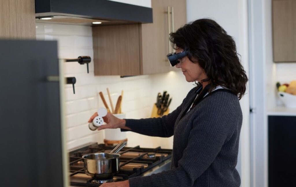 woman seasoning some food in a pot on the stove while wearing the eSight glasses