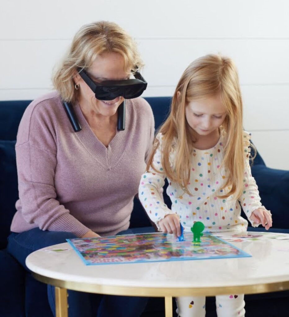 woman sitting next to her daughter on a blue couch playing a board game wearing the eSight glasses